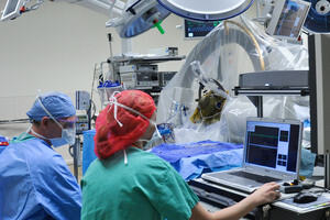 Scene from a surgical procedure with three medical professionals in full surgical garb and a patient undergoing a scan.