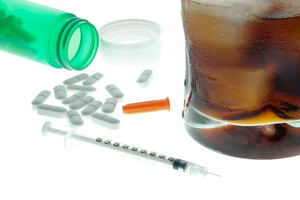 pills, a syringe and a rum and coke on a white table